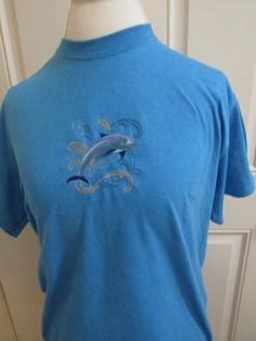 "Our \"Dashing Dolphin\"  embroidered T-Shirt is a great choice for that ocean or beach lover in your life. The dolphin design is embroidered  and is approximately 4\" x4\" and is centered on the shirt. The shirt is Gildan 50% cotton and 50% polyester pre shrunk blue heather.  The shirt comes in small, medium large and extra large.  I offer it in other colors but please ask me as some of the colors do not display the dolphin well." Blue Custom Embroidery Short Sleeve Top, Blue Short Sleeve Top With Custom Embroidery, Embroidery Dolphin, 2000s Dolphin Aesthetic, Embroidered Short Sleeve T-shirt For Beach, Embroidered Cotton T-shirt For Beach, Dolphin Embroidery Pattern, Embroidered Short Sleeve Beach T-shirt, Beach Embroidered Short Sleeve T-shirt