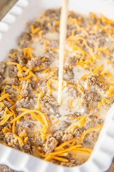 a casserole dish with cheese being drizzled over the ground beef