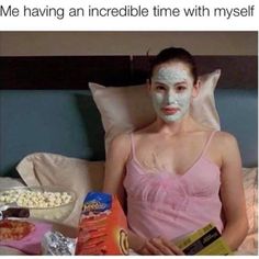 a woman laying in bed with her face mask on while holding a box of popcorn