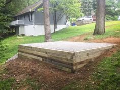 a wooden platform sitting in the middle of a yard next to some trees and grass