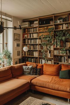 an orange couch sitting in front of a book shelf filled with lots of books and plants