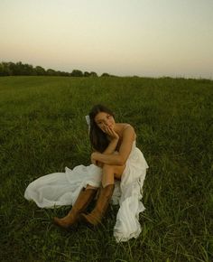 a woman sitting in the grass with her head on her hand