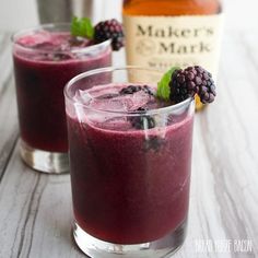 two glasses filled with berry and blackberry smoothie next to a bottle of maker's mark