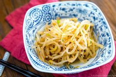 a blue and white bowl filled with noodles on top of a wooden table next to chopsticks