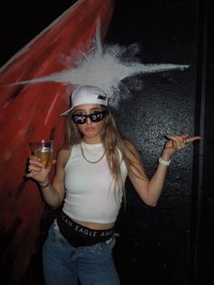 a woman wearing sunglasses and holding a glass in her right hand while posing for the camera