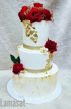 a three tiered white cake with red roses on the top and gold trimmings