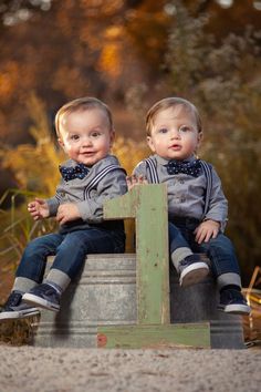 two young boys sitting on top of a metal bucket in front of some grass and trees