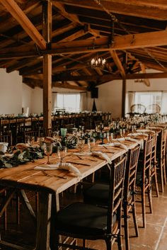 a long wooden table with place settings and greenery on it in a large room