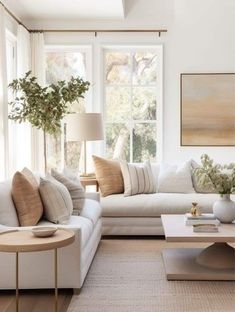 a living room filled with white furniture and lots of pillows on the couches in front of large windows