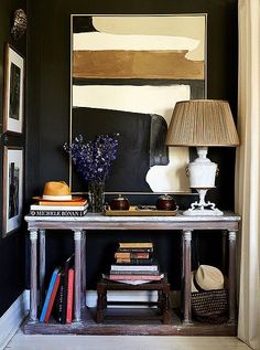 a table with books and a lamp on it in front of a large framed painting