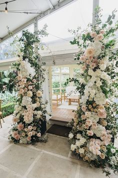 an indoor wedding ceremony with flowers and greenery on the arch, decorated in white and pink colors