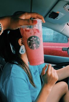 a woman sitting in the driver's seat of a car holding a drink