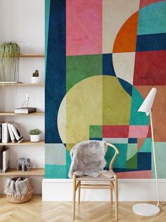 a chair in front of a colorful wall with bookshelves on the side and a lamp next to it