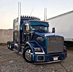 a large blue semi truck parked in front of a white trailer behind it's door