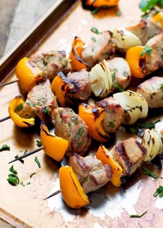 a wooden cutting board topped with meat and veggies on skewered skewers