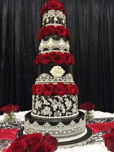 a three tiered wedding cake with red roses on the bottom and white lace around it