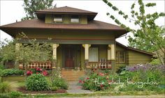 a green house with red trim and flowers in the front yard on a sunny day