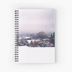 a snow covered field with trees and buildings in the background spiral notebook on white paper