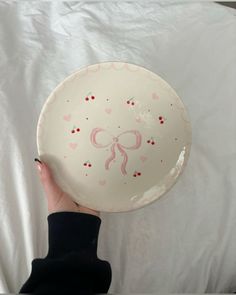 a hand holding a plate with pink bows on it and hearts painted on the side