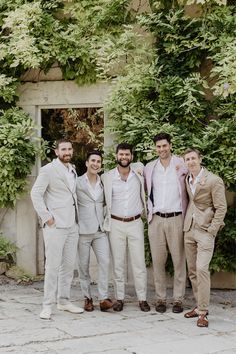 a group of men standing next to each other in front of a green plant covered wall