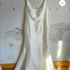 a white wedding dress hanging on a hanger in front of a wall with peeling paint