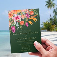 a person holding up a card with flowers on it in front of the ocean and palm trees