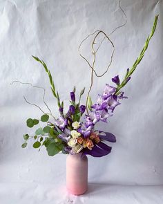 a pink vase filled with purple flowers and greenery on top of a white surface