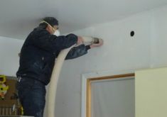 a man is using a vacuum to clean the walls in his house while wearing a protective mask