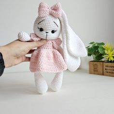 a crocheted bunny doll being held by someone's hand on a table