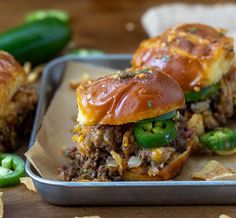 two sloppy joes sitting on top of a tray next to green peppers and jalapenos