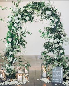 a wedding arch with candles and flowers on the table in front of it is decorated with greenery