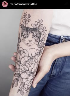 a woman with a cat and flowers tattoo on her arm, holding onto the arm