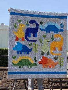 a person holding up a quilt made to look like dinosaurs