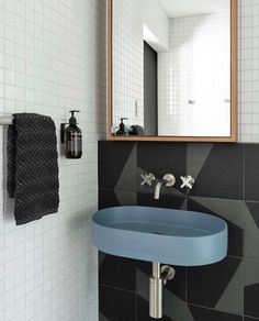 a bathroom with black and white tiled walls, blue sink and wall mounted mirror in the corner