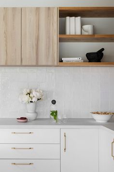 a white kitchen with wooden cabinets and flowers in vases on the counter top next to it