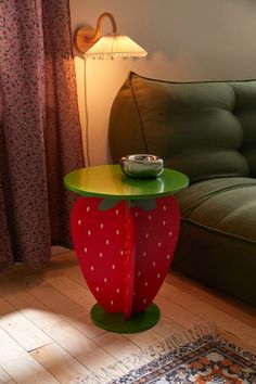 a strawberry shaped table sitting on top of a wooden floor next to a green couch