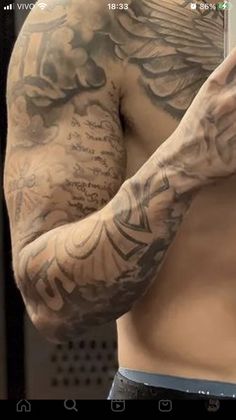 a man with tattoos on his arms and chest holding a cell phone up to his face