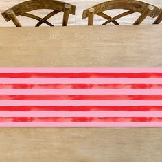 two wooden chairs sitting next to each other on top of a pink and red background