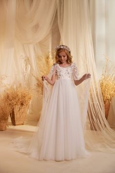 Elevate your little girl's special occasion with the stunning Pentelei Couture 3624 Communion Dress. This exquisite gown features a 3D floral attached cape in sheer fabric embellished with shimmering crystals and pearls, adding a touch of glamour to her look. The floral bodice creates a sweet and charming appeal, while the sheer floor length layered tulle skirt adds a soft and ethereal touch. Perfect for a flower girl or communion ceremony, this dress is sure to make your little princess feel li Communion Dresses Catholic, Confirmation Dresses, Girls Communion Dresses, Lace Cape, Flower Girl Crown, Layered Tulle Skirt, Girls Pageant Dresses, Christening Dress, Couture Dress