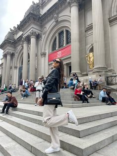 a woman standing on steps in front of a building with people sitting and walking around