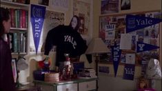 a woman standing in front of a desk with books on it and several pennants hanging from the wall