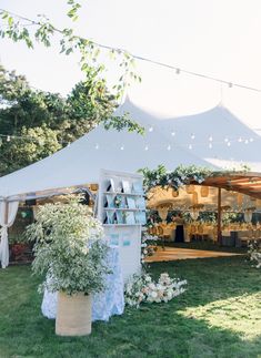 an outdoor tent set up with tables and chairs in the grass, surrounded by greenery