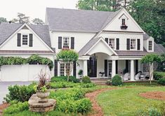 a large white house with black shutters and lots of greenery in the front yard