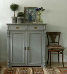 an old gray cabinet with flowers on top and a chair in the corner next to it