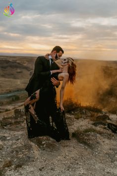 a man and woman standing on top of a rocky hill next to an open field