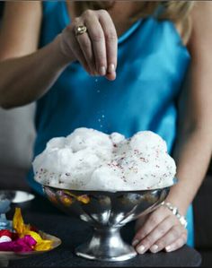 a woman sprinkling sugar on top of a cake in a silver bowl with confetti