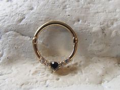 a gold ring with black and white stones on it sitting against a stone wall in the snow