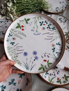 a person holding a plate with flowers painted on it and other plates in the background