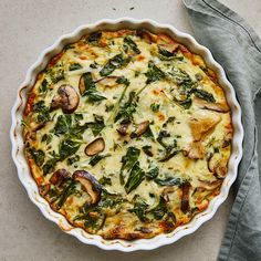 a quiche with spinach, mushrooms and cheese in a pie pan on a table