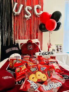 a bed topped with lots of red and black balloons next to a table filled with snacks